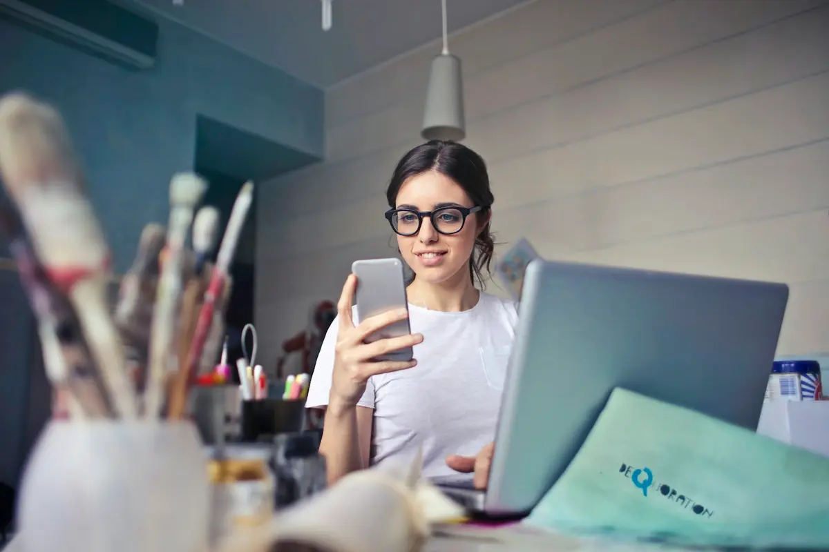 Corretora usando o celular à mesa de trabalho, com o notebook aberto
